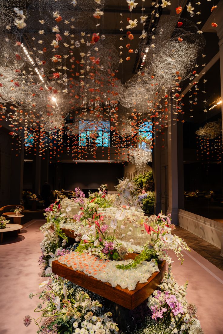 Fleurs suspendues au plafond au-dessus d’un buffet fleuri, dans une salle sombre