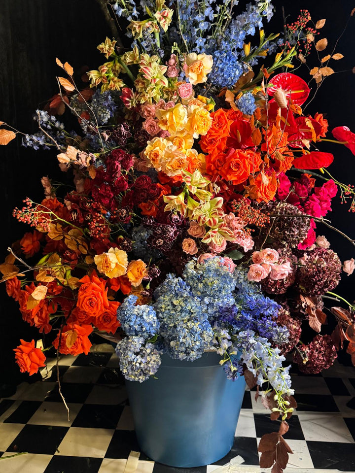 La composition du cadre doré de près : roses orange, dahlias, delphiniums bleus et hortensias dans un vase bleu