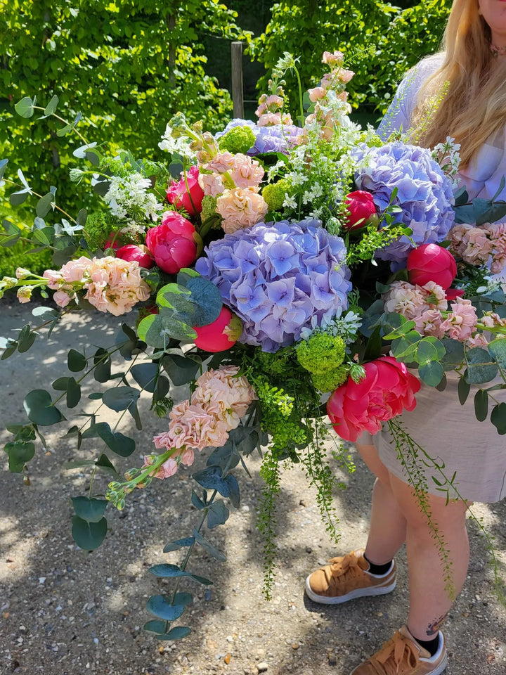 Bouquet rond d’hortensias bleus, de pivoines et de feuillages, dans un jardin