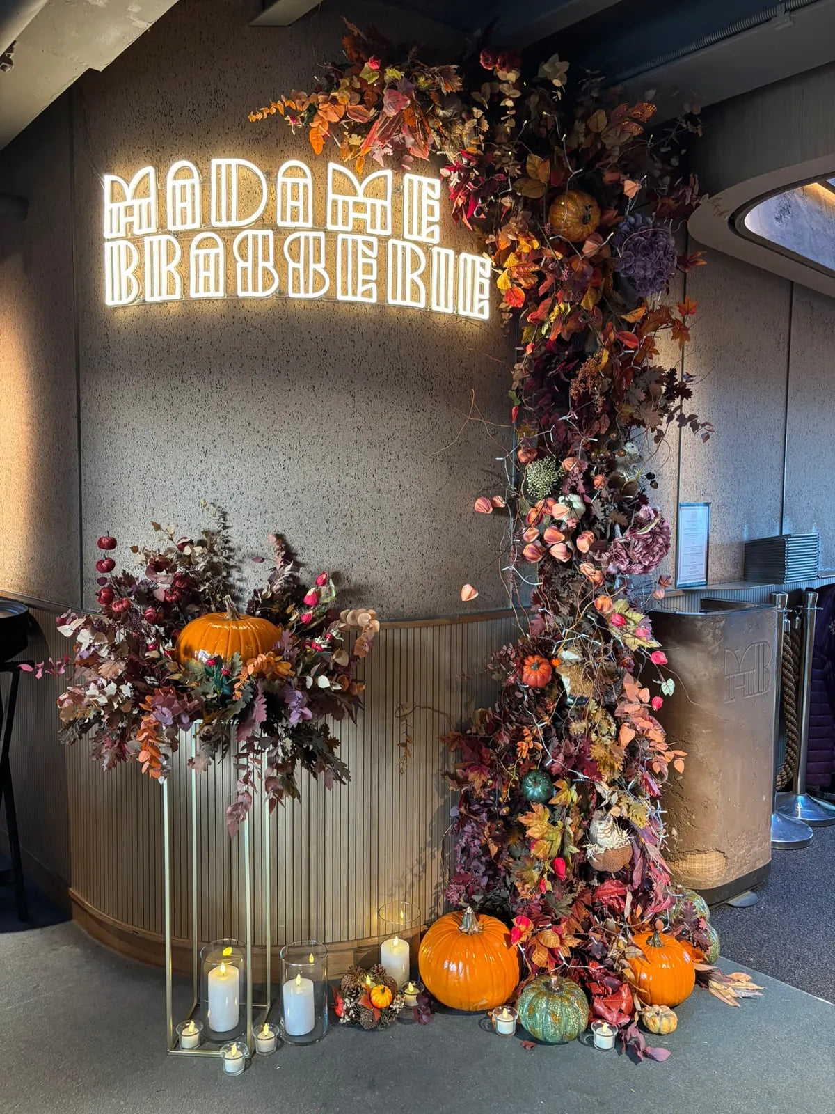 L’entrée de Madame Brasserie décorée pour l’automne : colonne de feuillages autour de l’enseigne lumineuse, citrouilles et bougies au sol