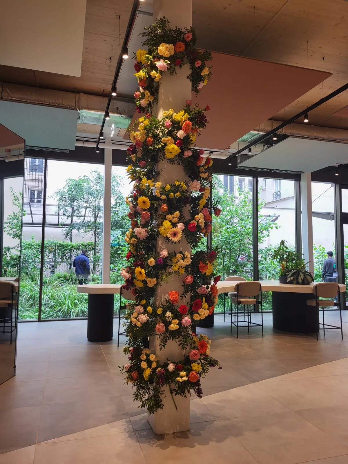 Pilier du hall habillé de gerberas jaunes et de roses, devant une baie vitrée